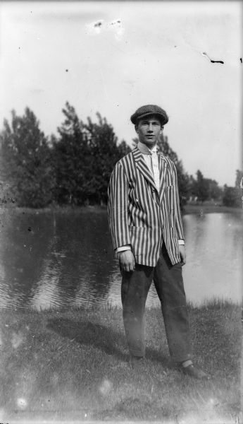 Forest Middleton poses near a body of water wearing his University of Wisconsin freshman's blazer and a cap.