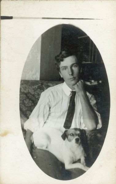Photographic postcard of Forest Middleton, with a pensive expression with hand on his chin, sits with his dog in his lap.