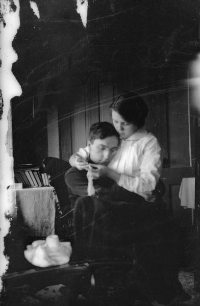 Forest Middleton, wearing eyeglasses, holds Leonore Judkins Middleton on his lap. She is crocheting as he rests his head on her bosom.