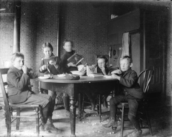 Forest Middleton, second from right, and four other boys, enjoy apples and popcorn in the Middleton family kitchen. One boy is peeling an apple as another empties the corn popper. Forest is looking at a book with a bird illustration in it.