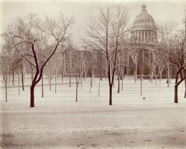 A winter scene with the third Wisconsin State Capitol from the east.  There is snow on the ground and clinging to the trees.