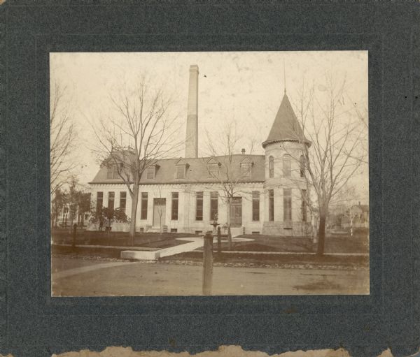 The Madison waterworks building, with corner tower and turret. The building was located at the corner of Gorham and Livingston Streets.  The large smokestack was required for the steam powered pump that maintained water pressure. There is a fountain with statue in front of the building.