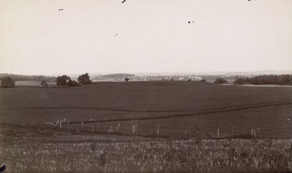 A rural landscape with large fields in the foreground and a small town with church in the background.