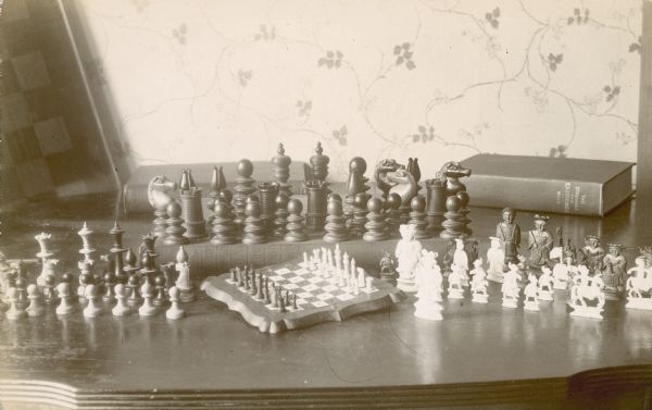 A collection of chess sets displayed on a table with Walter Thomas Mills' 1904 book "The Struggle for Existence."