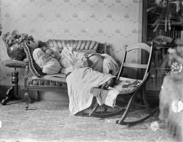 Clara Middleton lies on a love seat with her feet supported on a folding rocking chair.