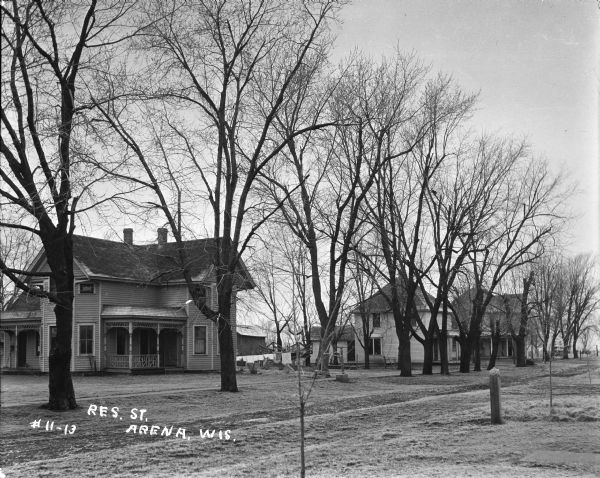 View across dirt road of homes among trees. View features three residential dwellings, each featuring two stories and porches.