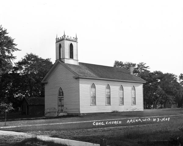 Exterior view of the Congregational Church, featuring the church building with arched windows, an arched entrance, a chimney, and a bell tower.