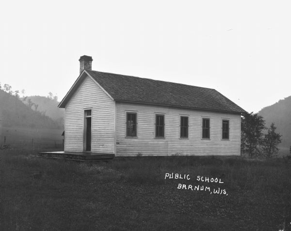 Exterior of a one-room schoolhouse surrounded by rural landscape.