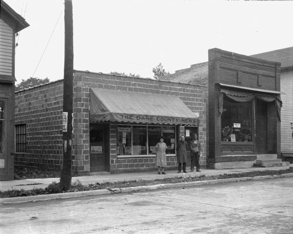 View from street of three people posing in front of the printing office and shop.