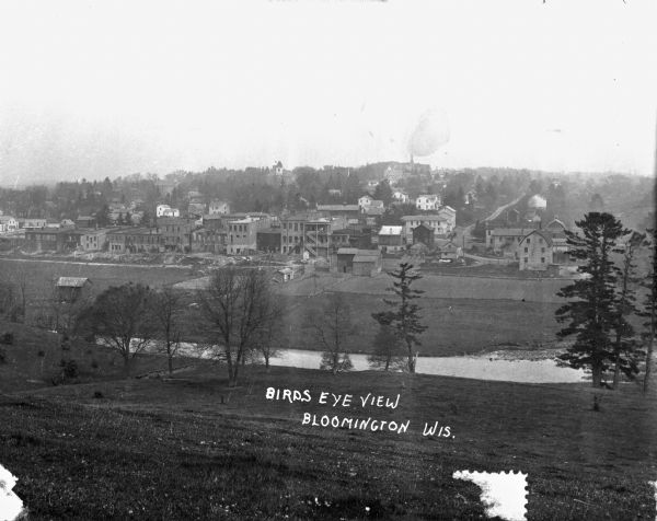 Bird's-eye view of Bloomington. In the open space, there are trees and a creek. In the developed area, there are stores, apartments, and barns. The buildings are mostly multi-storied.