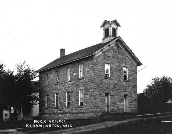 The two-story stone schoolhouse. A flagpole hangs over the entrance.