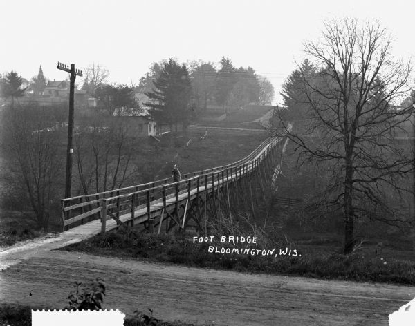 A woman stands on a wooden footbridge. There are homes in the distance.