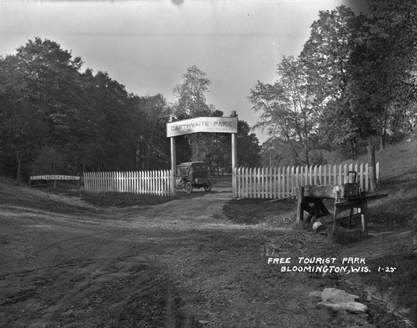 The entrance to the Carthwaite Park tourist camp and picnic grounds. There is a sign for a filling station 1 mile ahead. A car is parked inside the grounds.