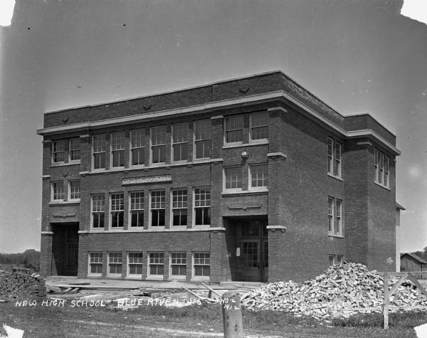 Exterior of high school. The sign on the building reads, school - 1911. Construction debris litters the front of the building.