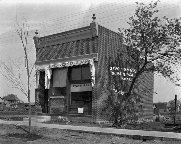 The exterior of Blue River State Bank. Thorough the front window a man can be seen at his desk.