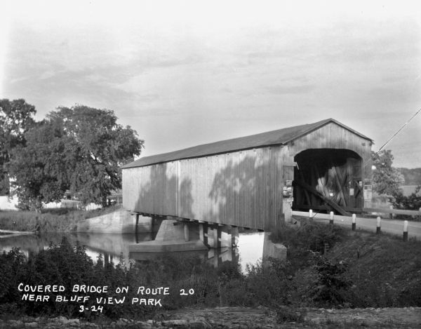 View from shoreline of a covered bridge over a river.
