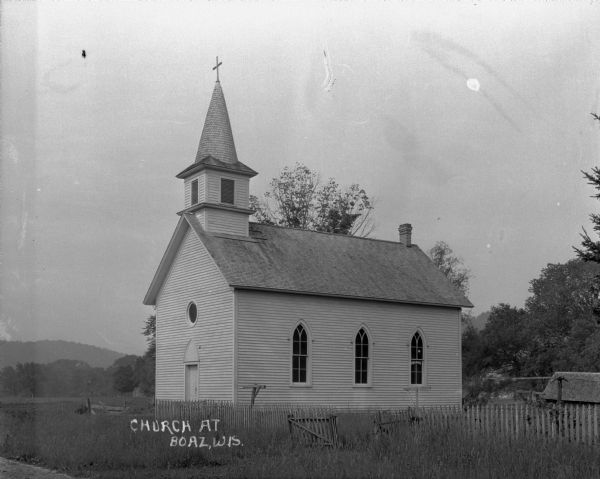 Exterior of a church with a steeple, cross, lancet arched windows and door.