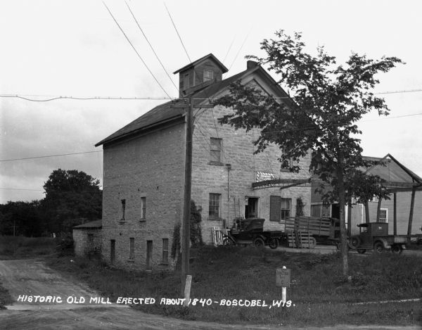 Exterior of a feed mill erected About 1840. There is an advertisement for Quaker Ful-O-Pep feed above the entrance. Two pickup trucks are parked outside.