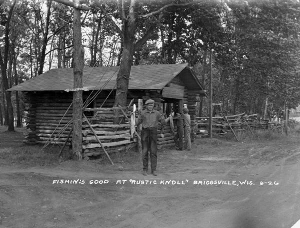 A man poses holding a fish in both hands. Two boys wait at the service window of a log cabin.