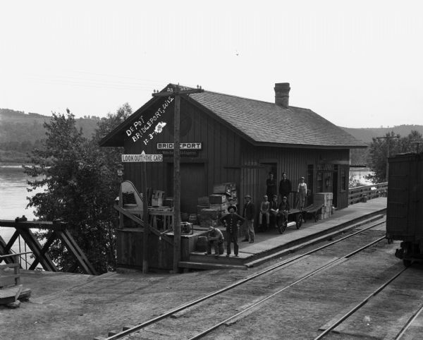 Elevated view of the Bridgeport depot on the Wisconsin River. A group of men and boys pose on the platform. There is a Wells Fargo Company Express sign below the depot's name.