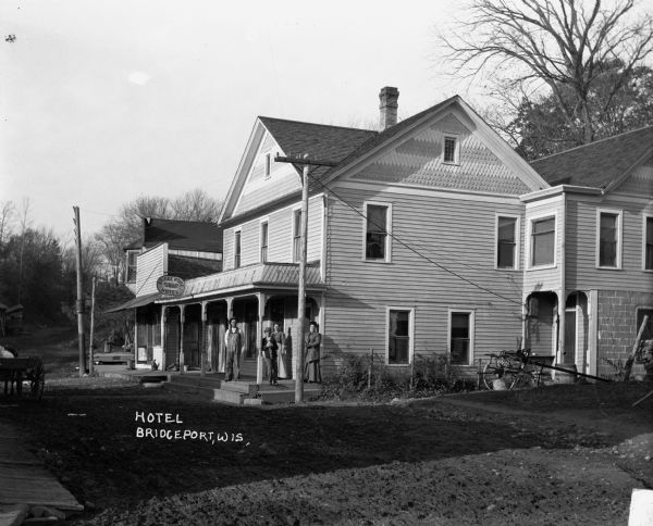 The exterior of the Bridgeport Hotel. A man, boy, dog, and two women stand on the porch.