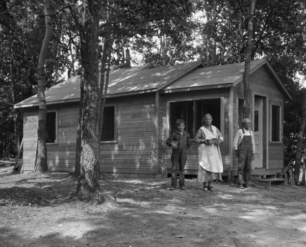 A mother, father, and son pose outside of a cabin at Amacoy Lake Resort. The woman and boy are holding pint berry boxes of fruit.