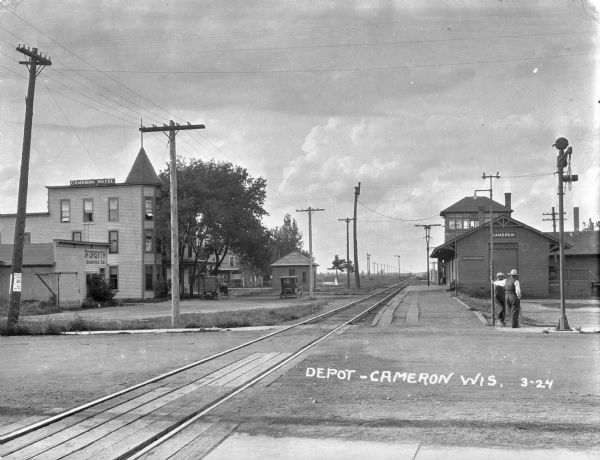 The Cameron train depot near the Cameron Hotel and the Forsyth Construction Company. Two men stand by the platform.
