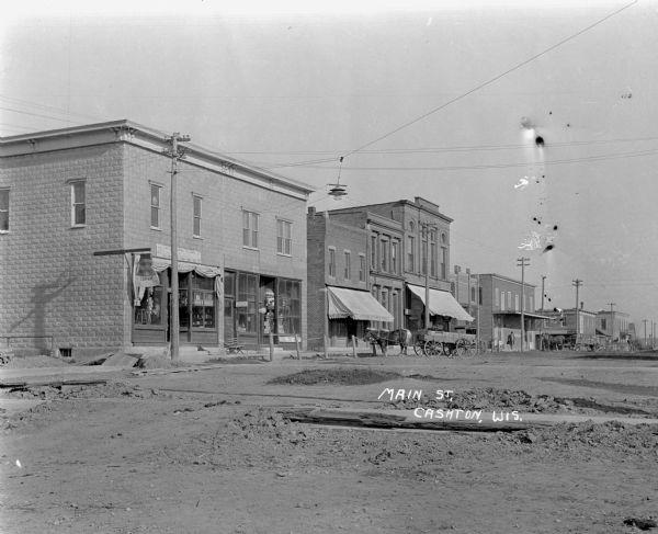 View across unpaved street of a row of stores. On the corner is the Cashton Hardware Company. A horse and wagon is parked at the curb of H. B. Bohl City Meat Market.