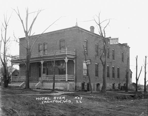 Exterior view of the Hotel Byer, which features two stories, a balcony, a porch, and two hanging signs on utility poles.