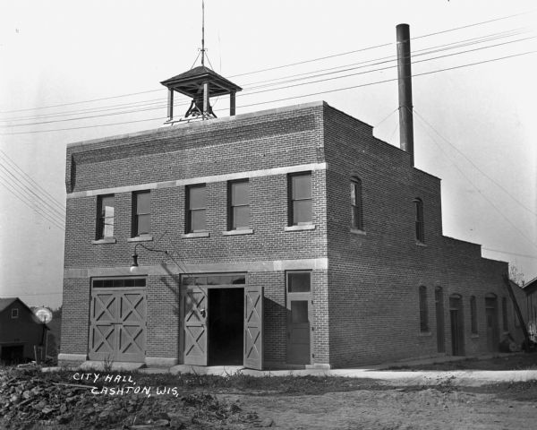 Exterior of city hall. The brick building features two sets of double doors, a bell tower, and a tall chimney.
