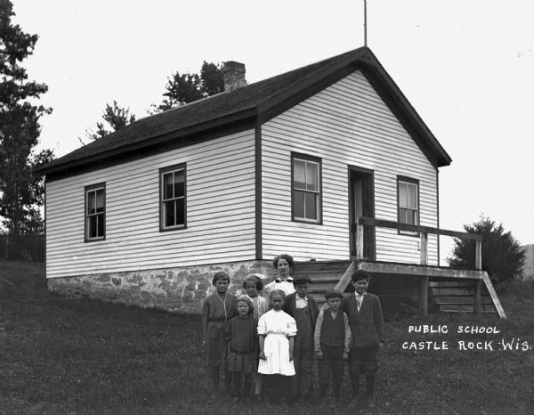A class of students and their teacher pose outside of the public school.