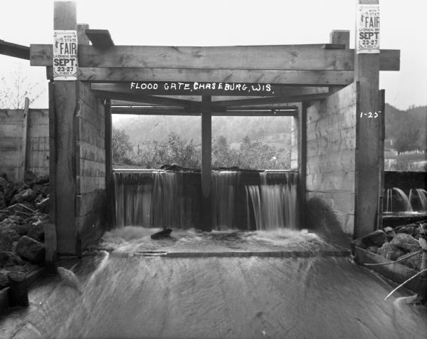 Wooden flood gate with water pouring out. There are signs on either post advertising the interstate fair in La Crosse on September 23-27.