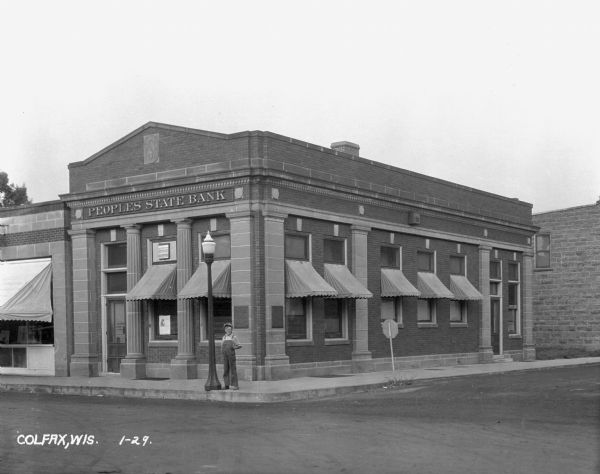A boy stands at the corner in front of the Peoples State Bank.
