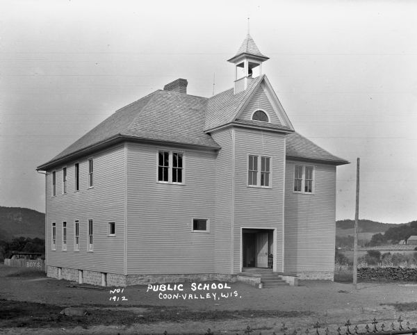 Exterior of the school, which has a bell tower. The word "boys" is painted on a fence behind the school