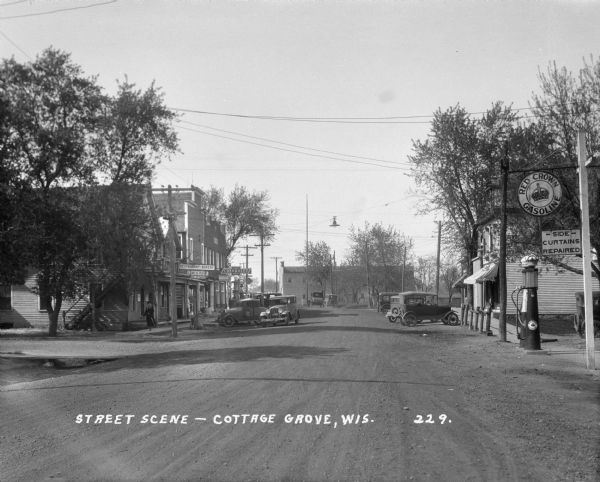 View down a road towards commercial strip of town. On the right is a gas station and repair shop, on the left side are a restaurant/bakery, and a Chevrolet/Pontiac repair shop and gas station.
