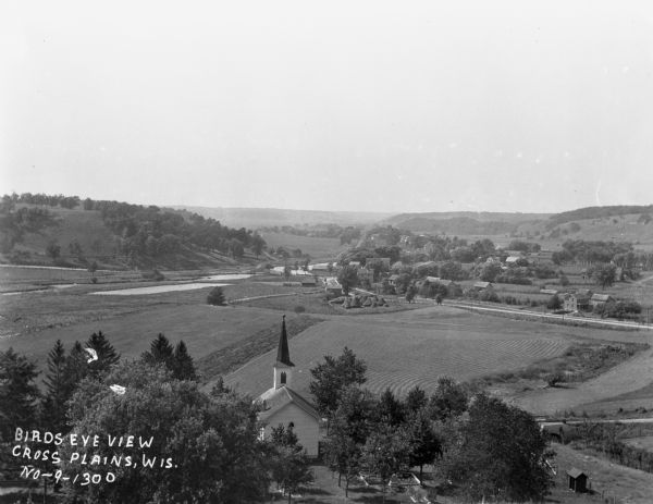 View from hill over church and cemetery towards fields and town in a valley.