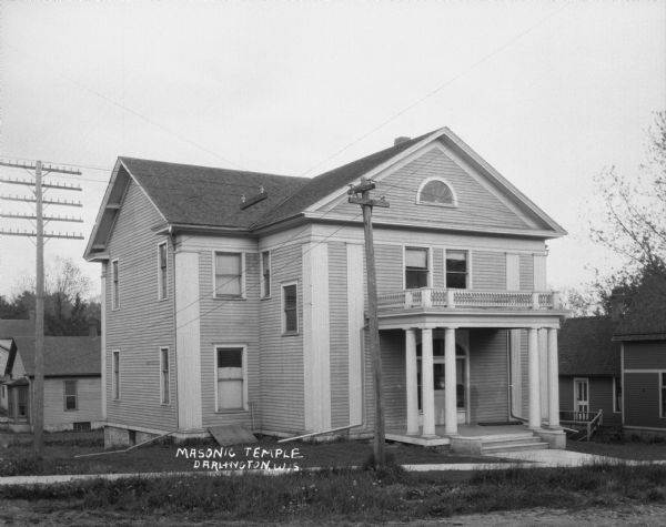 Exterior view of the Masonic temple. The facade features a balcony, columns, and a cross gable roof.