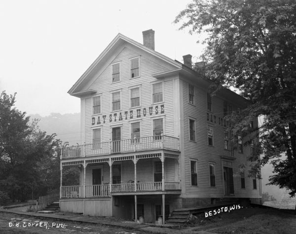 Exterior view of the Bay State House hotel. The building features three stories, a porch, a balcony, and a gable roof.