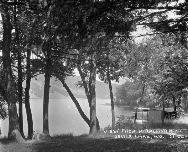 View of Devil's Lake from the shore of the Kirkland Hotel, located at the southeast corner of the lake. There is building, perhaps a boathouse, on the shore near the boats and boating docks.