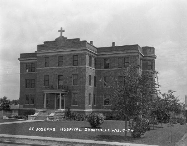 Elevated view of exterior of Saint Joseph's Hospital. The three-story building has a cross on the roof over the entrance.