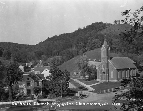 Elevated view of the Catholic church, residential homes, with hills and trees in the background.