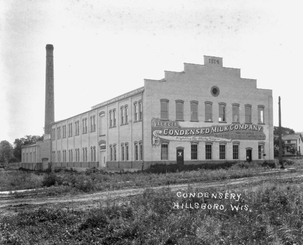 Exterior of the Valecia Condensery Milk Company factory. The company's sign is painted on the crow-stepped gable wall of the factory. The sign reads, "Valecia Condensery Milk Company - Manufacturers of the Valecia Process Sterilized Evaporated Milk - Lighting The Milky Way."