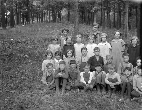 An off-centered group portrait of schoolchildren and an adult female in a forest setting.
