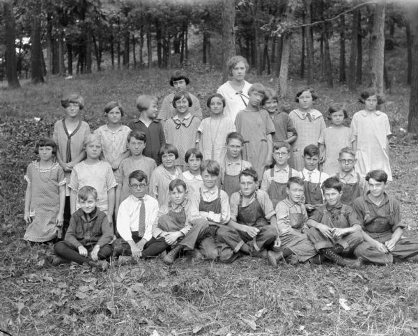 Group portrait of schoolchildren with an adult female in a forest setting.