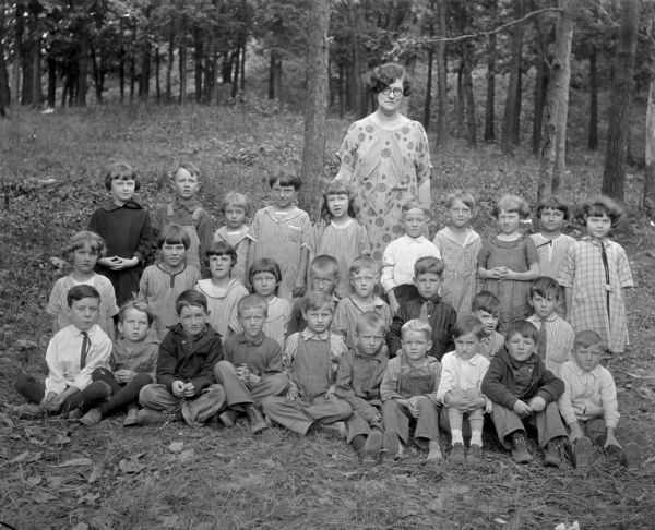Group portrait of schoolchildren with an adult female in a forest setting.