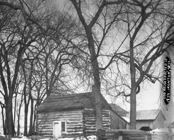 Exterior view of a log cabin and other housing structure in the background.