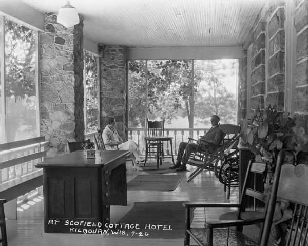 A man and woman sit across from one another on an enclosed porch at the Scofield Cottage Hotel.