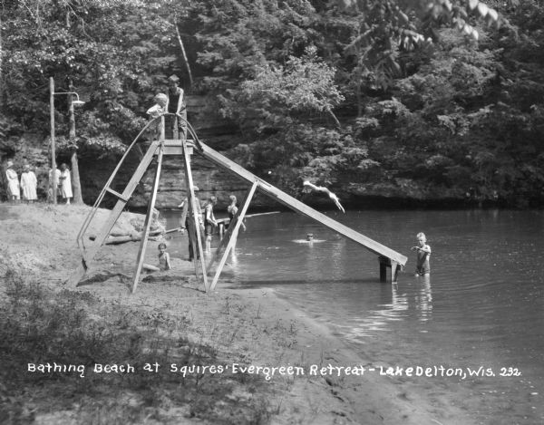 Beach at the Squires' Evergreen Retreat. Two children stand at the top of the water slide while others play in the water.