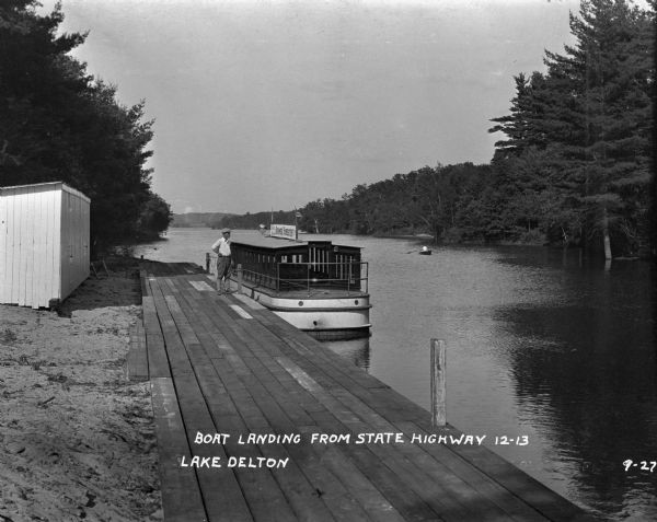 A man stands on a wooden dock near a tour boat. The sign on top of the boat advertises "Summer Homesites."