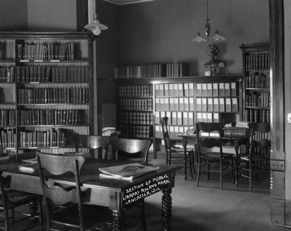 Interior of the public library. The room contains tables and chairs, a bust sculpture of a woman, and bookshelves.